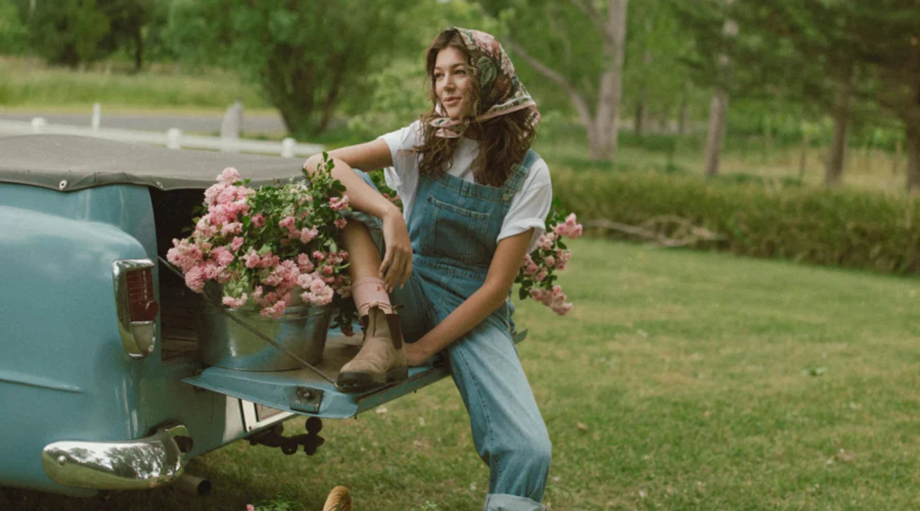 Woman sitting on back of ute surrounded with a bucket of pink flowers wearing FARMER brand clothing